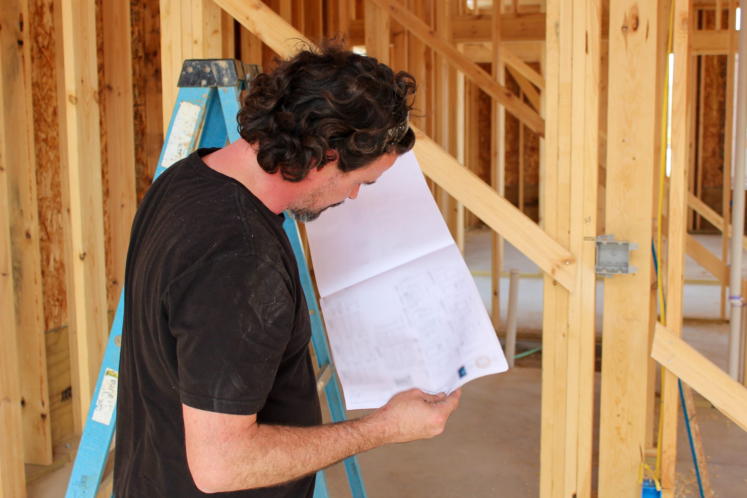 Electrical contractor reviewing blueprint for electrical wiring installation in framed house