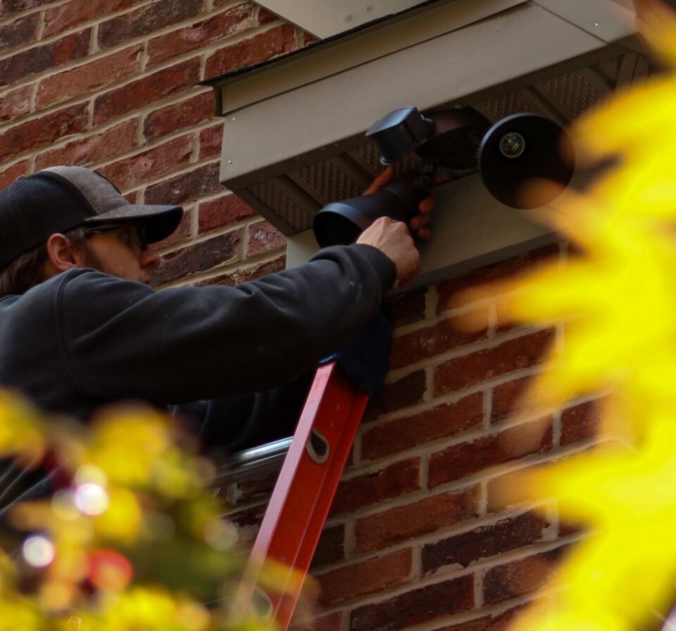 Contractor installing spotlights on side of residential home for enhanced outdoor lighting