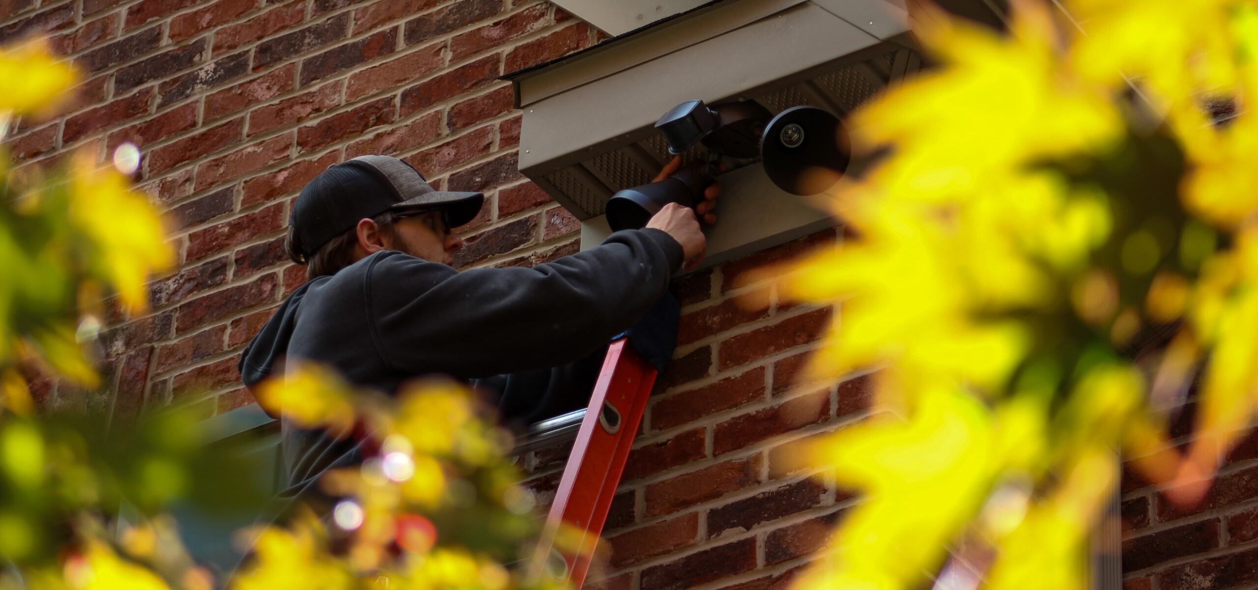 Contractor installing spotlights on side of residential home for enhanced outdoor lighting