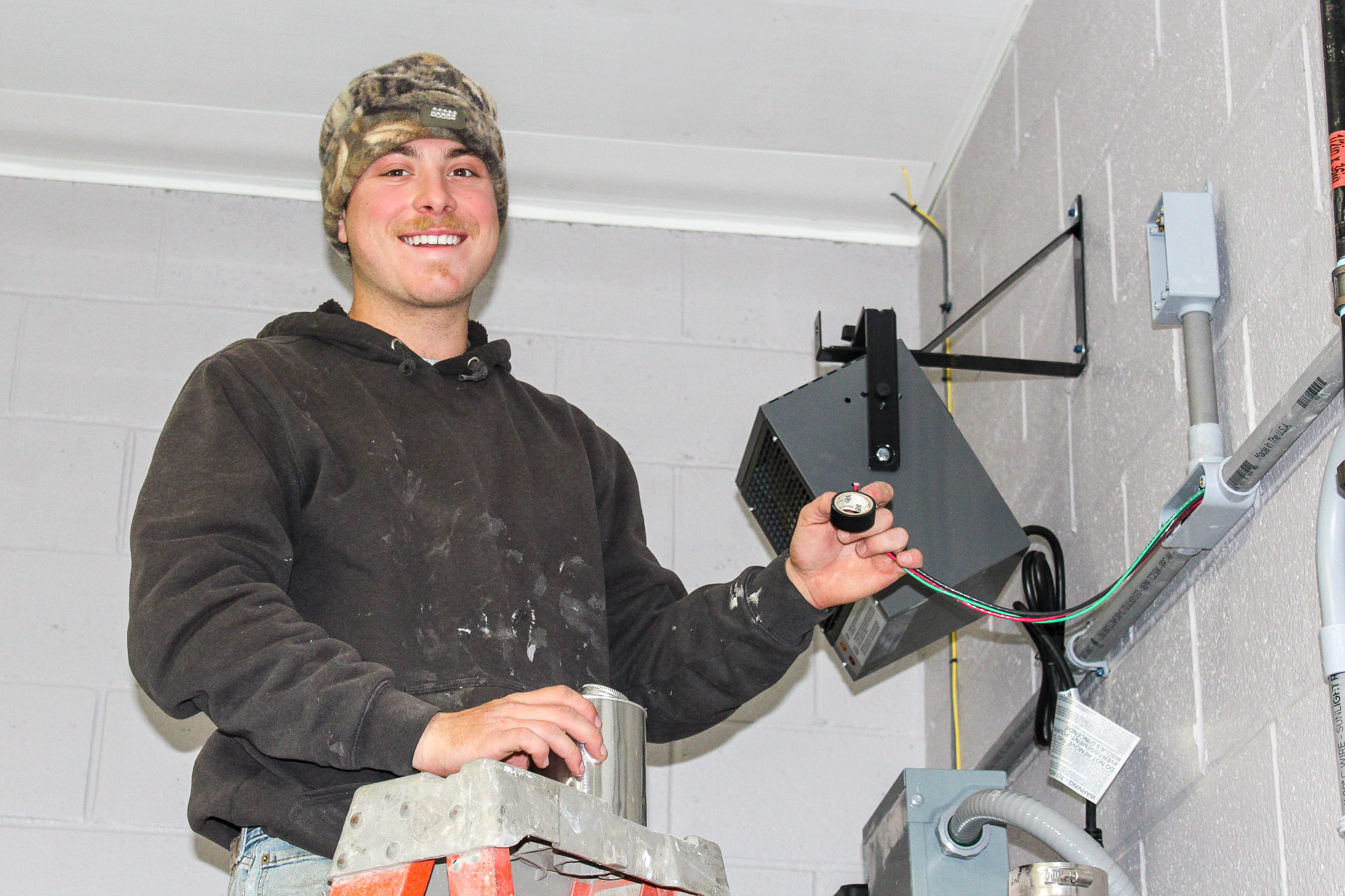 Electrician on a ladder installing wiring for a heater demonstrating expert electrical craftsmanship and safety compliance